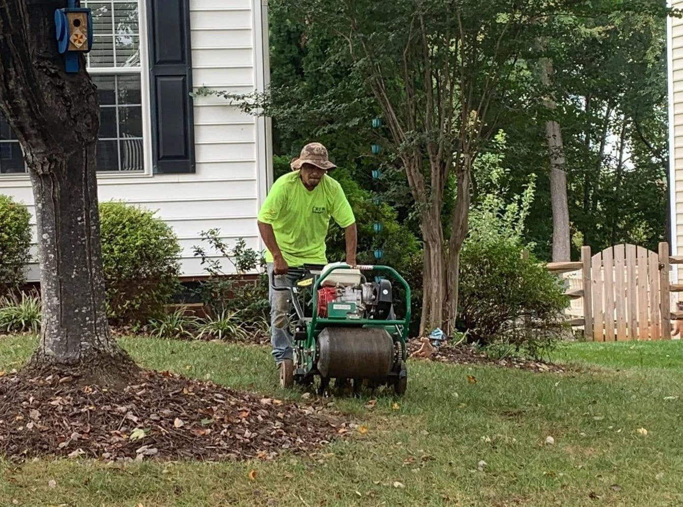 Crew member running a core aerator across a front lawn