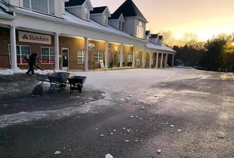 Crew member clearing snow from a storefront walk at dawn