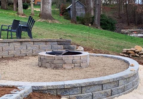 Block fire pit ring on a gravel patio inside a curved seating wall